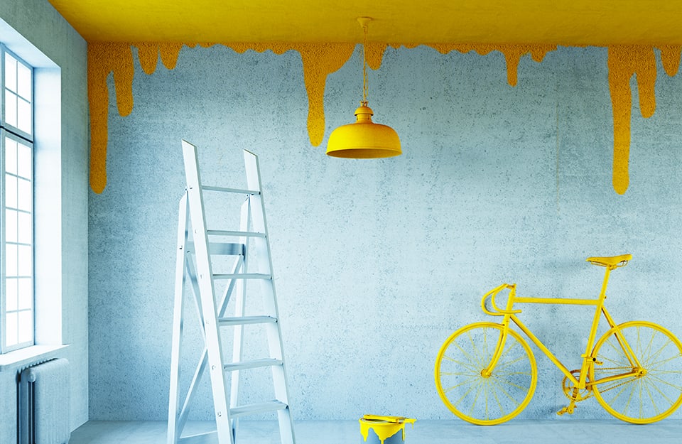 Stanza vuota che inizia a essere dipinta di giallo. Si vede il colore che goccia dal soffitto sulle pareti, che sono ancora grezze. C'è una scala e ci sono un lampadario giallo, una bicicletta gialla e un secchio di vernice gialla