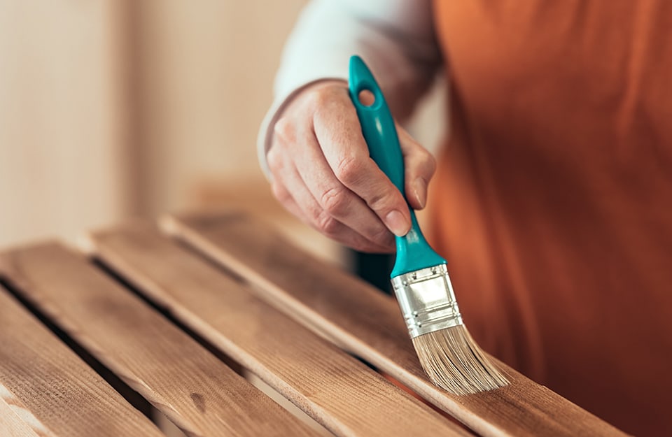 Primo piano sulla mano di un uomo che sta dando una seconda o terza mano di mordente a una superficie in legno