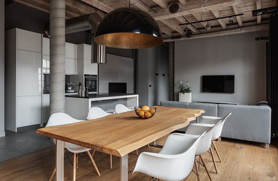 Open space soppalcato con sala da pranzo e grande tavolo in legno naturale con sedie di design, su parquet, sotto un grande lampadario industrial nero