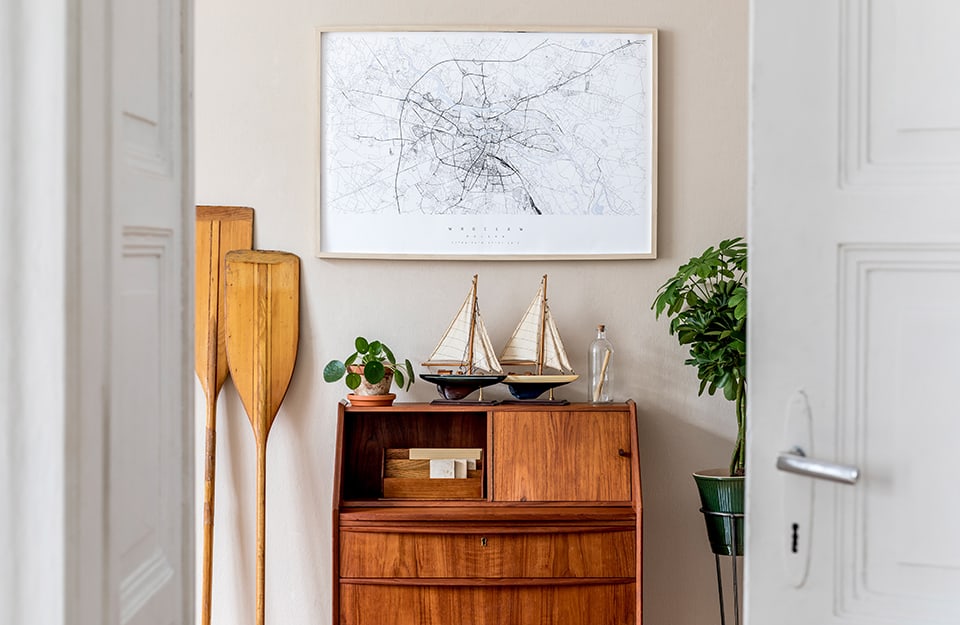 Entrance with a natural wood console-desk, with model sailing ships on it, a painting with a map and canoe oars next to it. Two open white doors frame the scene;