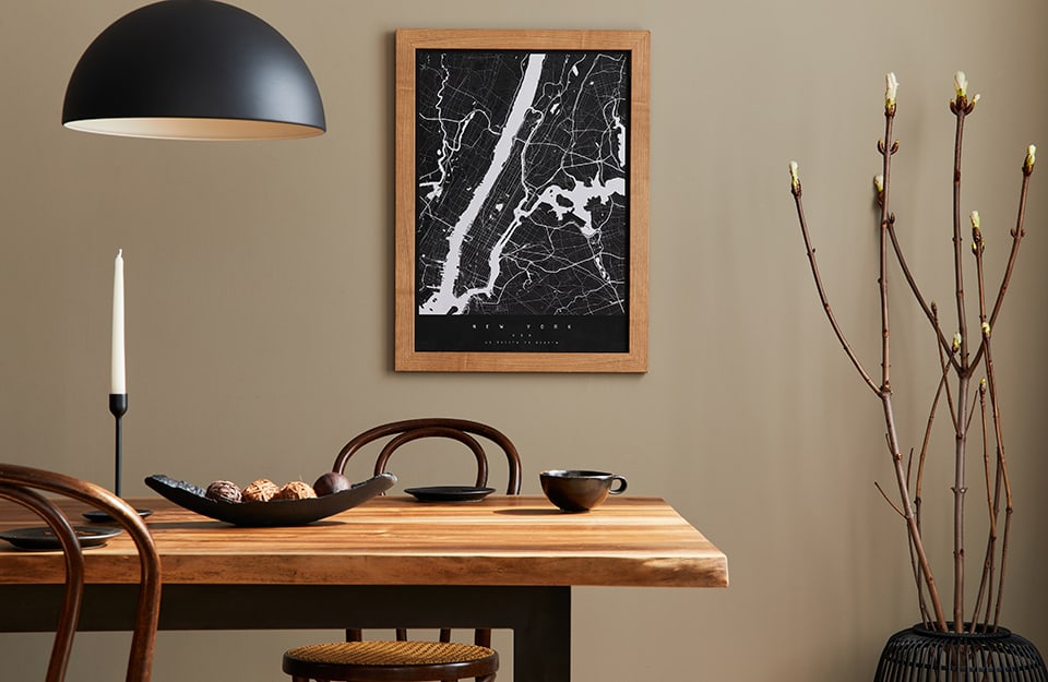 Detail on a rustrial dining room table with a natural wood surface. A black semi-sphere chandelier descends from the ceiling. On the wall is a framed black and white map