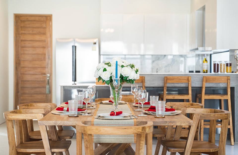 Festively decorated dining table in natural wood. A natural wooden door and a kitchen in shades of white and grey can be seen behind it;