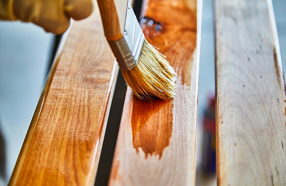 Primer plano de un cepillo que está pasando impregnante sobre unos elementos de madera