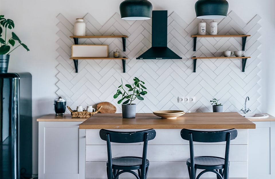 Cocina moderna de estilo vintage, con taburetes pintados de verde, pared de azulejos, paredes blancas, color de acento verde y estantería de madera natural