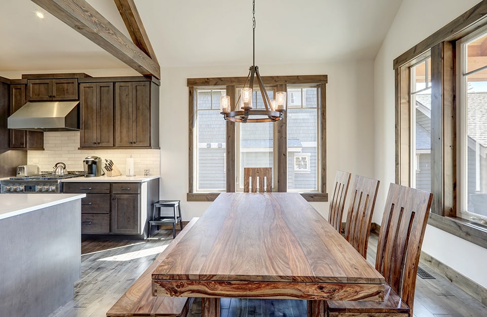 Espacio abierto con cocina y luminoso comedor de estilo rústico, con una larga mesa de madera con veta vista, a un lado sillas altas del mismo estilo y al otro un largo banco;