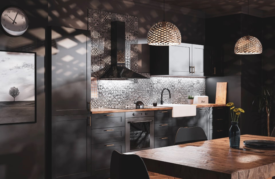 Vista angolata di una cucina nera, con paraschizzi in maioliche bianche e nero ed effetti di luce dati dai lampadari in vimini intrecciati