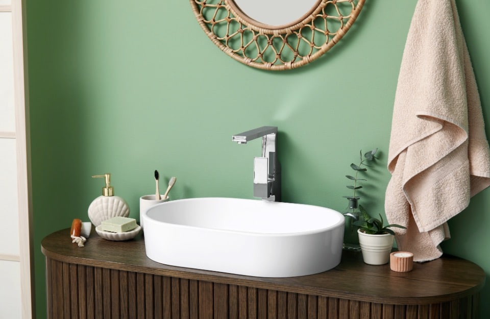 Detail of a white oval-shaped ceramic sink in a bathroom with mint green walls