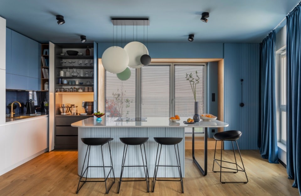 Una cocina moderna con isla. La habitación está amueblada con diferentes azules, blancos, negros y madera natural