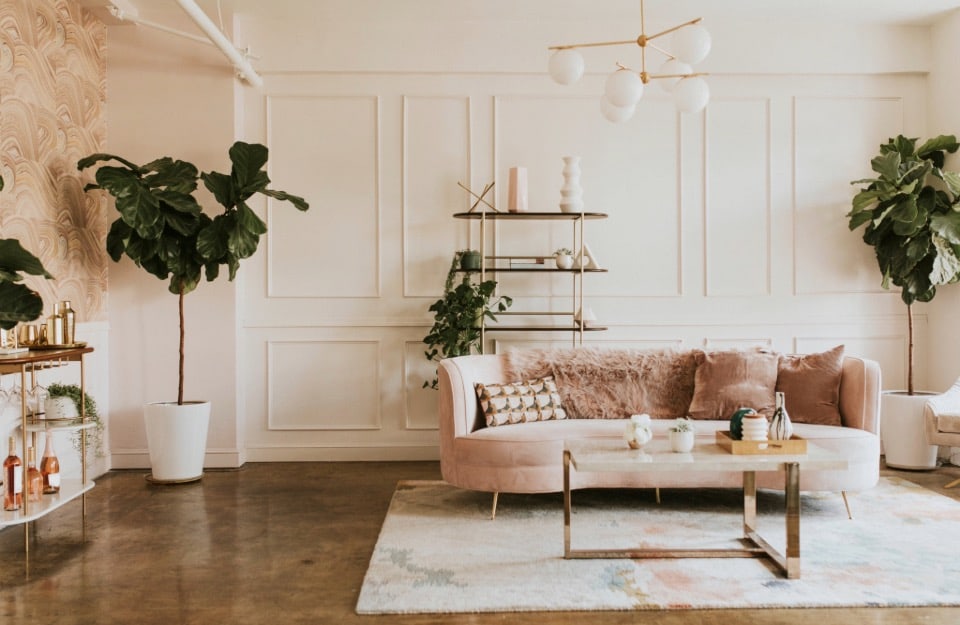 Salotto in stile glam, con divano rosa in velluto, tavolino da caffè con struttura dorata, lampadario da soffitto anni '30, cuscini metallizzati